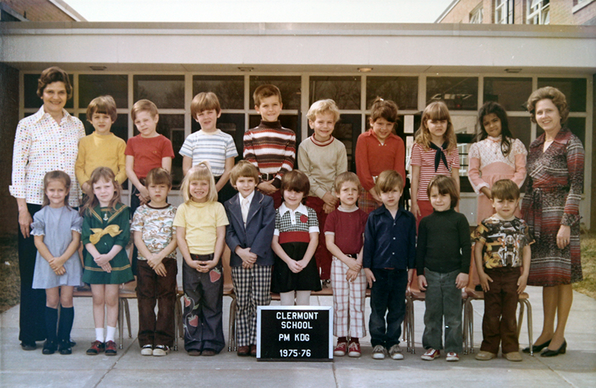Afternoon kindergarten class photograph taken during the 1975 to 1976 school year. 18 children and two teachers are pictured. They are posing on the sidewalk in front of the main entrance to the school.