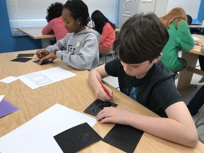 boy uses scratch tool to draw into scratchboard 