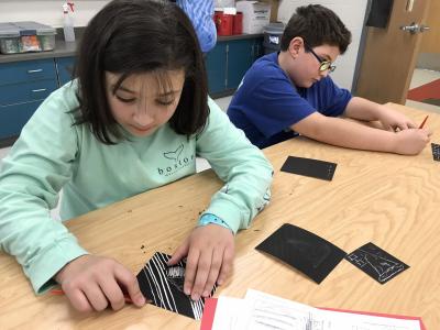 girl and boy creating a scratchboard drawing using scratch tools