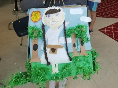 Student shows off her historical fiction bag project. She read "Journey to Nowhere". The bag shows her main character  created with paper and yarn