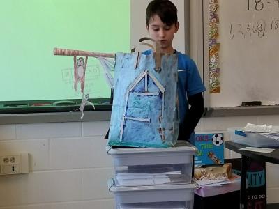 A student presents his historical fiction bag project. He shows off the bag depicting a "Magic Tree house Book"